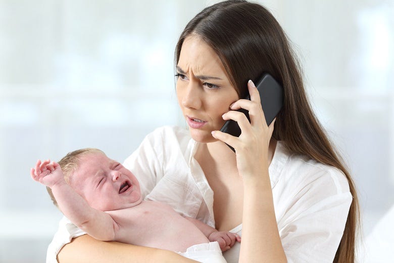 Mom on phone holding crying baby