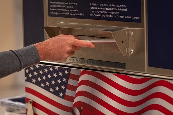A hand slides a ballot into a drop box