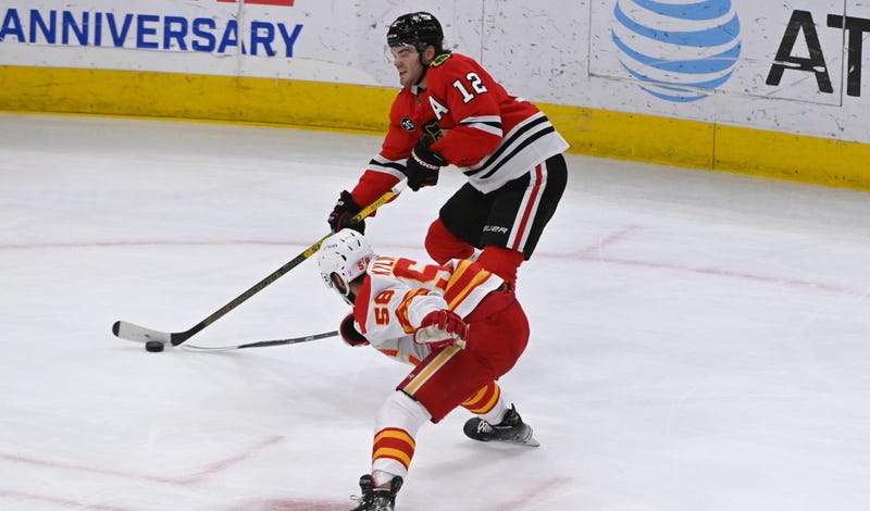 Blackhawks left wing Alex DeBrincat (12) moves the puck past Flames defenseman Oliver Kylington (58).