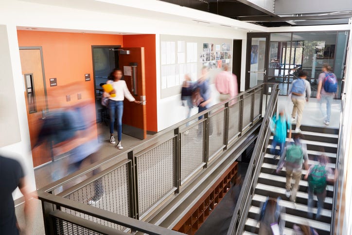 Blurred out high school students scurry through a hallway and up a flight of stairs