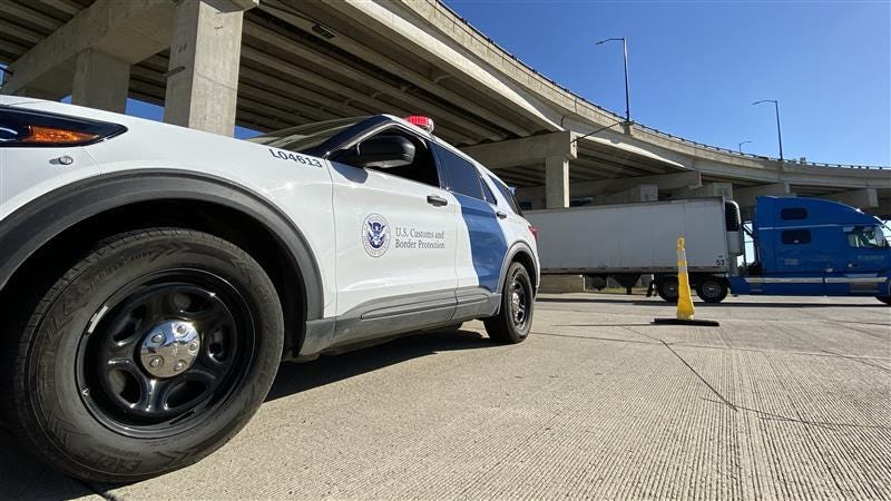 A marked CBP vehicle stationed in the outbound area of the Ambassador Bridge, with a semi-truck visible in the background.