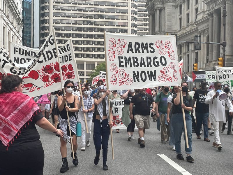 Marchers walk with a banner reading "Arms Embargo Now" past City Hall in Center City.