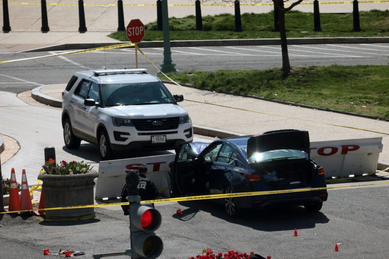 A damaged blue sedan in front of a police barricade at the U.S. Capitol.