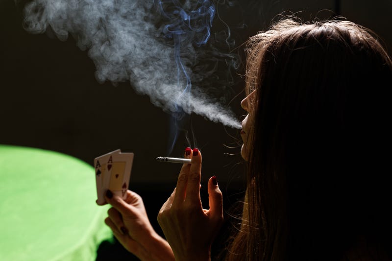 A woman smokes a cigarette while looking at a hand of cards.