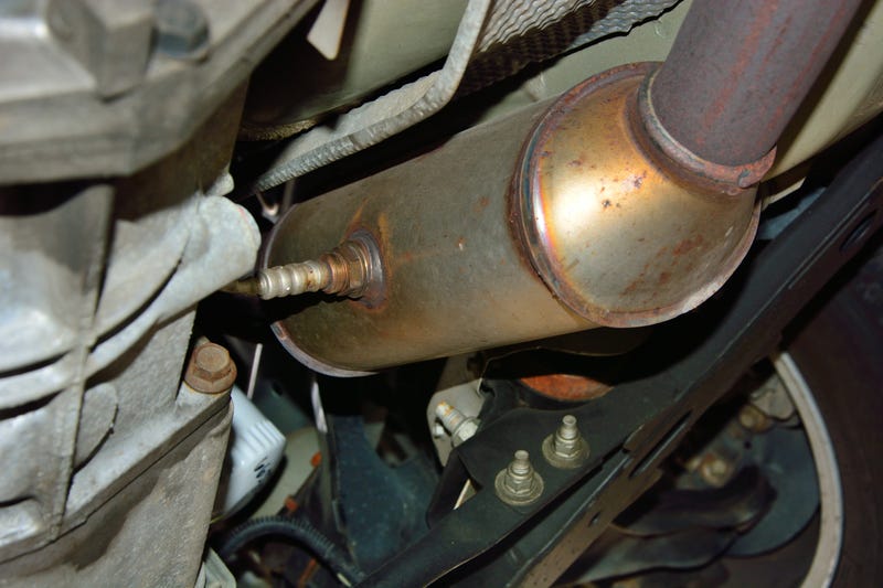 Selective focus on a stainless steel catalytic converter with an oxygen sensor or O2 sensor installed on an exhaust system under a vehicle.