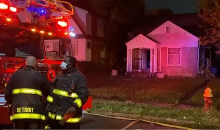 House after a fire has been put out. A fire truck with lights on and a fireman can be seen out front.