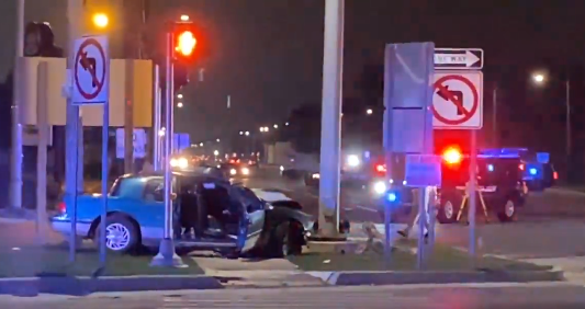 A 1992 blue Mercury Cougar crashed into a light pole. Police and other emergency response can be seen onsite.