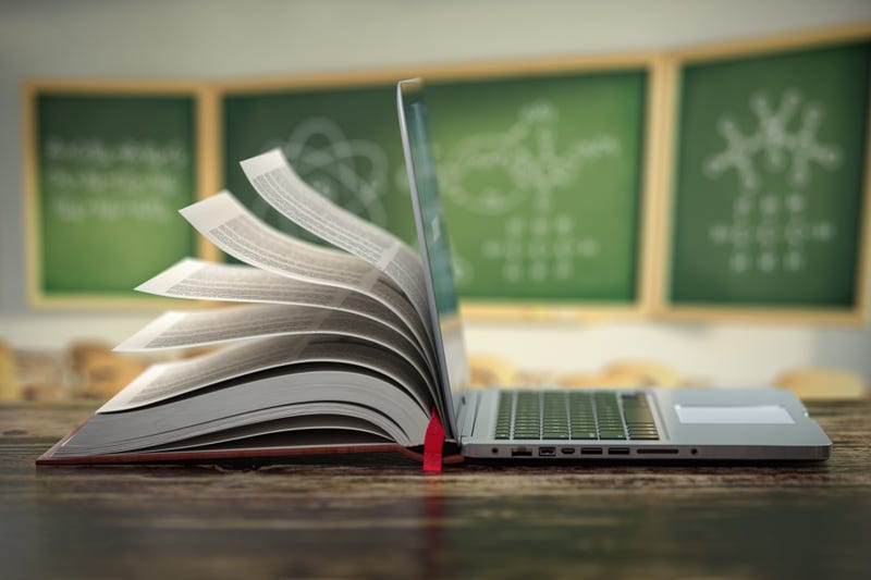 A book and laptop sit on a classroom desk