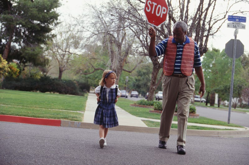 A crossing guard helps a young girl cross the street
