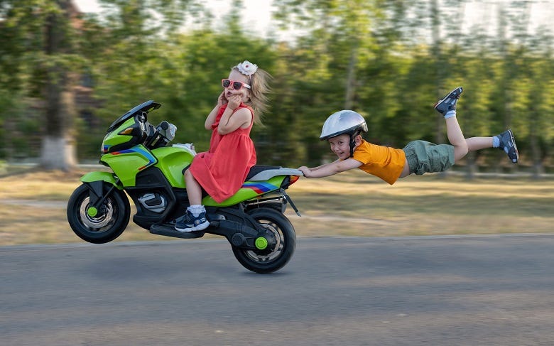 kid driving motorcyle with brother hanging off back