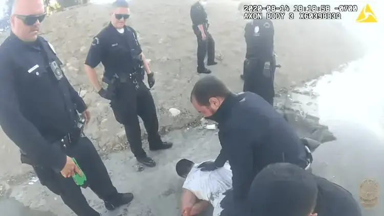 multiple police officers stand around while one kneels on the back of a man