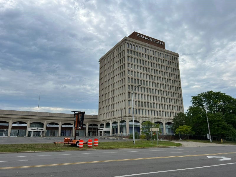 The vacant 12-story Village Plaza building. The lot is empty with the freeway running behind it.