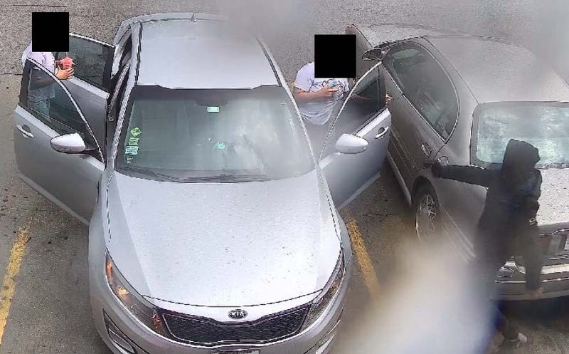 Man in black sweatshirt points gun at driver of vehicle as the driver and passengers exit the vehicle