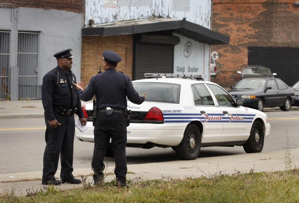 Two Detroit Police officers converse while standing near a patrol car