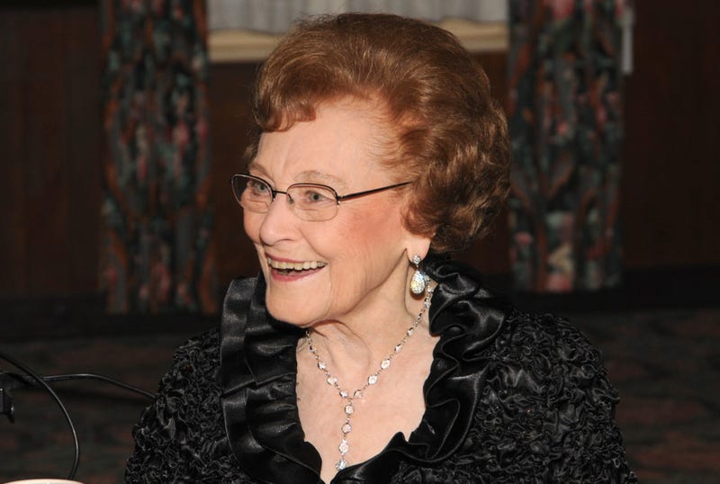 Photo of Dorothy Hecht Zehnder smiling, wearing a black top, dangling earrings and necklace 