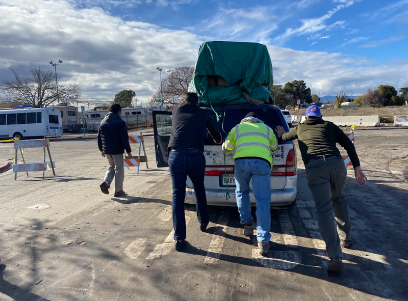 Encampment resident Sean Benak's broken-down car is moved with some helpers.