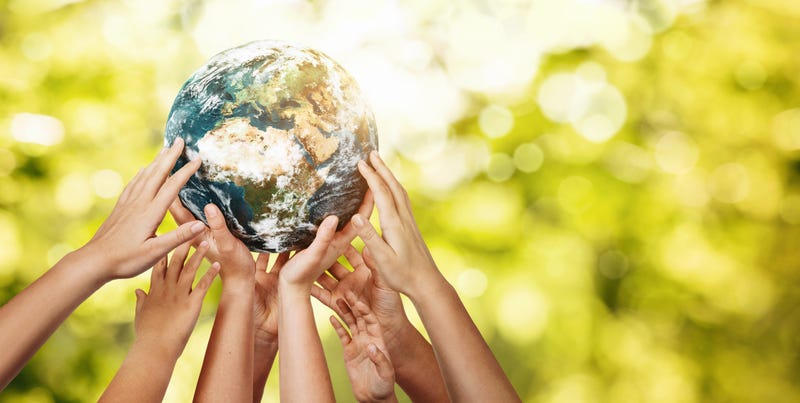 Group of children holding planet Earth over defocused nature background