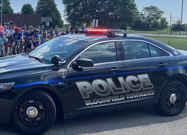 A Bloomfield Township police car are in front of a bunch of kids riding their bikes