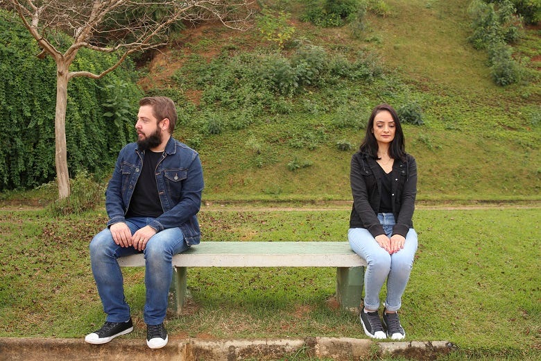 Couple sitting far apart on park bench 
