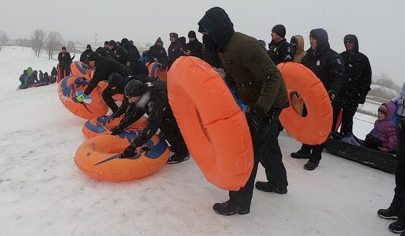 Police officers on snowy hill holding orange sled tubes 