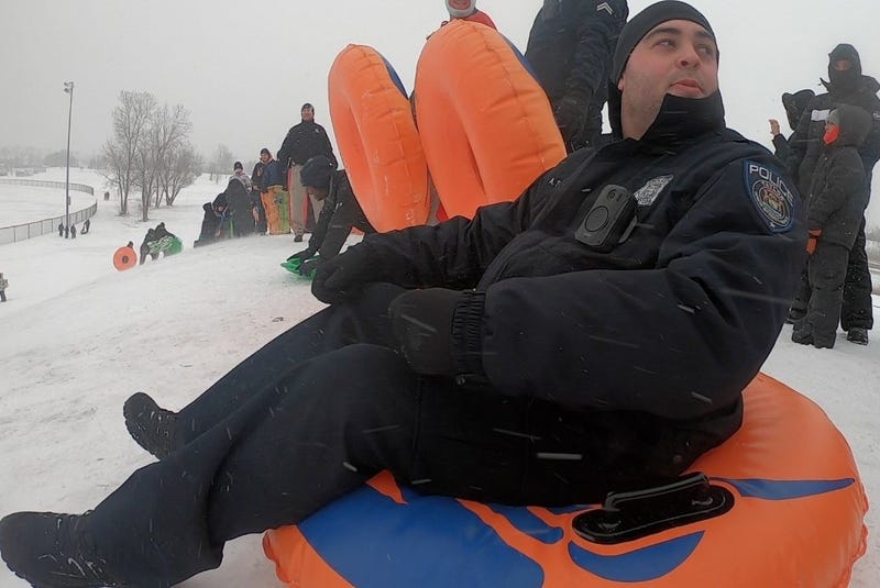 Police officer sitting on orange sledding tube on top of snowy hill 