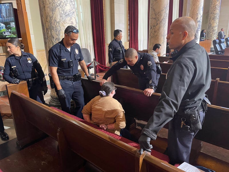 several police officers surround woman in city council chamber