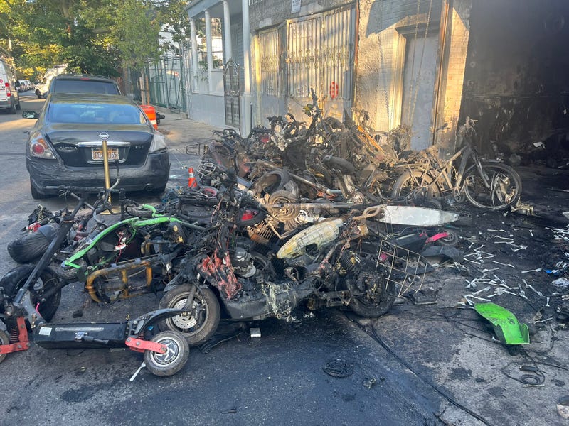 A pile of smoldering bikes and scooters is seen outside Kings Electric Scooters on Jamaica Avenue in Richmond Hill on Thursday morning