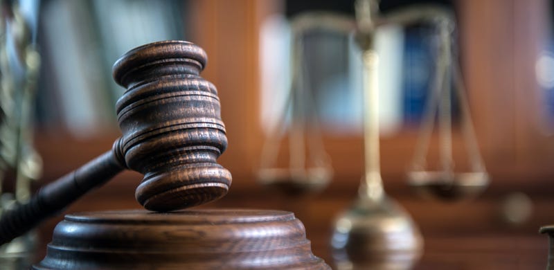 A judge's gavel, with the Scales of Justice in the background.