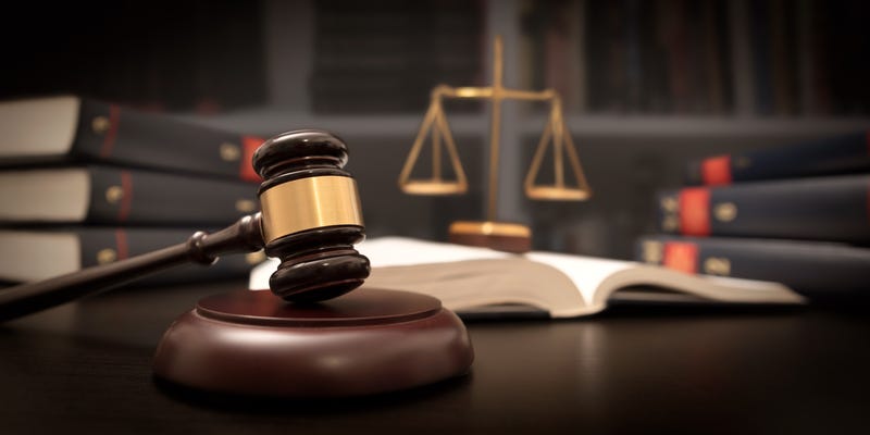 A gavel sits on a judge's desk, with the scales of justice in the background