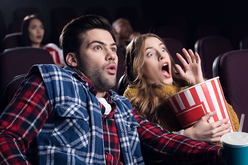 young shocked couple with popcorn watching movie in cinema