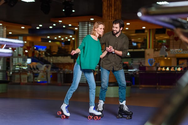Young couple holding hands while skating together on roller rink 
