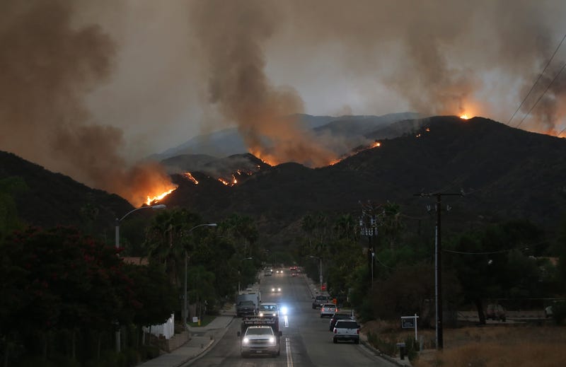 cars drive down road while wildfire burns in hills