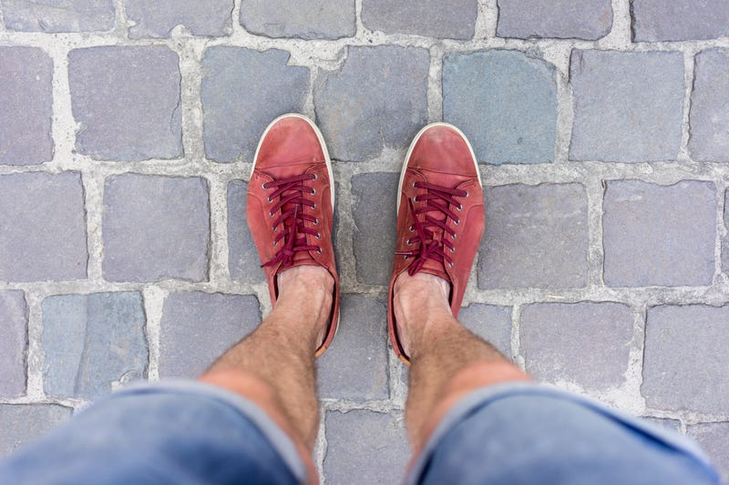 Man looking down at his legs and feet in red shoes.