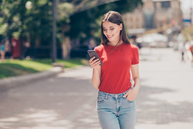 A woman walks smiling at her cell phone