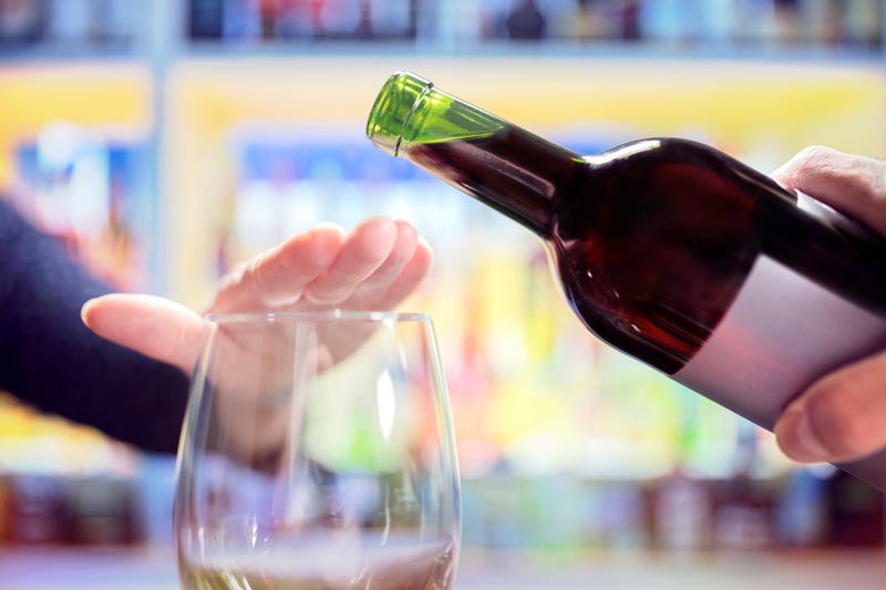 Woman's hand rejecting more alcohol from wine bottle in bar.