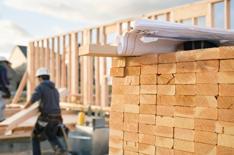 stacked wood in foreground, bones of a new house of wood in background