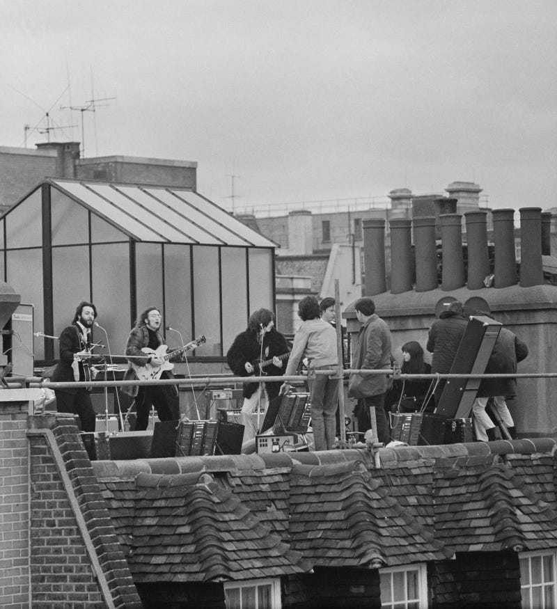 British rock group the Beatles performing their last live public concert on the rooftop of the Apple Organization building for director Michael Lindsey-Hogg's film documentary, 'Let It Be,' on Savile Row, London, UK, 30th January 1969; singer-songwriters Paul McCartney and John Lennon (1940 - 1980) perform at their microphones, and guitarist George Harrison (1943 - 2001) on the right. Lennon's wife Yoko Ono sits at right. (Photo by Evening Standard/Hulton Archive/Getty Images)