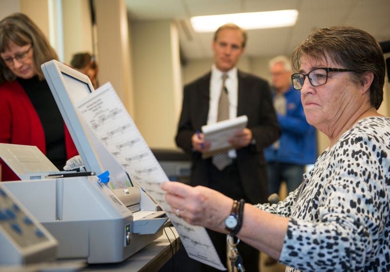 Election official Mary Wickersham (L) and Minnesota Secretary of State Steve Simon (C) look on as election official Mary Maynard enters selections into a voting machine during a public accuracy testing of Election Day voting machines.