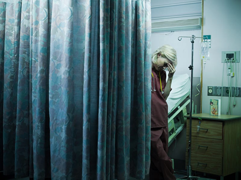 Sad nurse in hospital partially behind curtain.