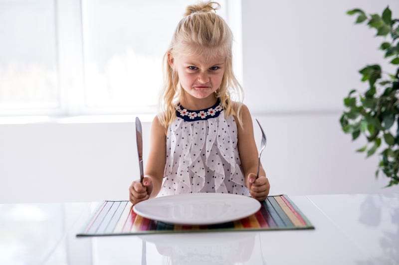 A Furious little girl waiting for dinner. Holding a fork in the hand