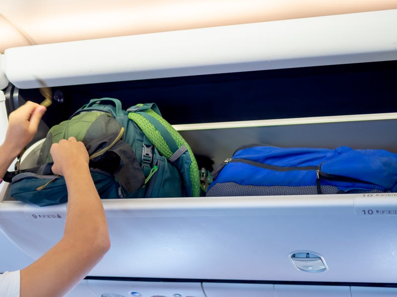 Man putting luggage in overhead airplane compartment stock photo.