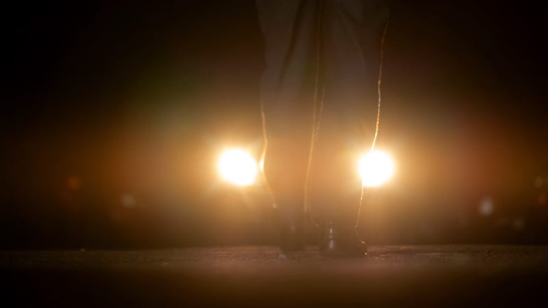 Person approaching a car with its headlights on.