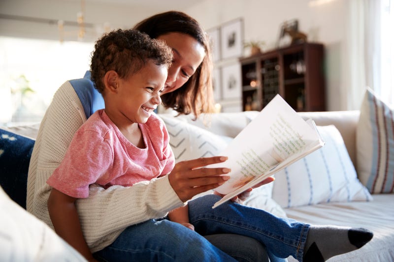 A woman holds a laughing child and a book on her lap