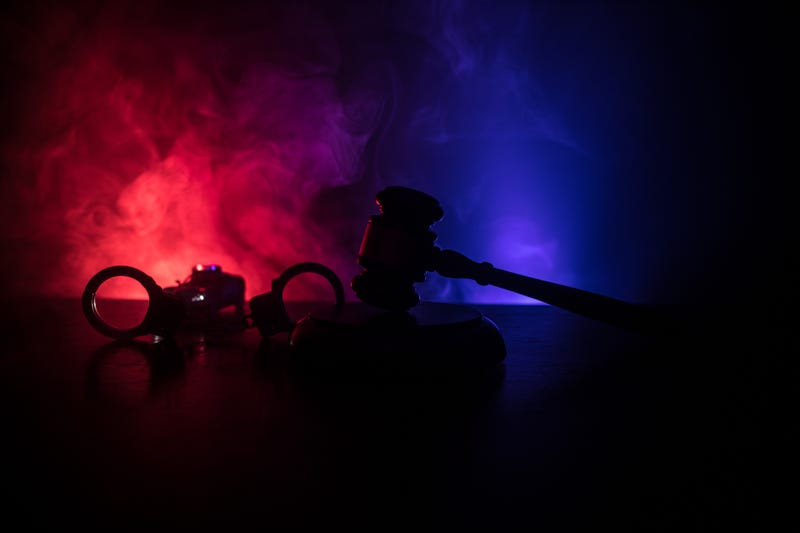 Law theme, mallet of the judge on wooden desk with Lady Justice Statue. Silhouette of handcuffs with police car on backside. Law gavel on dark foggy background with light.