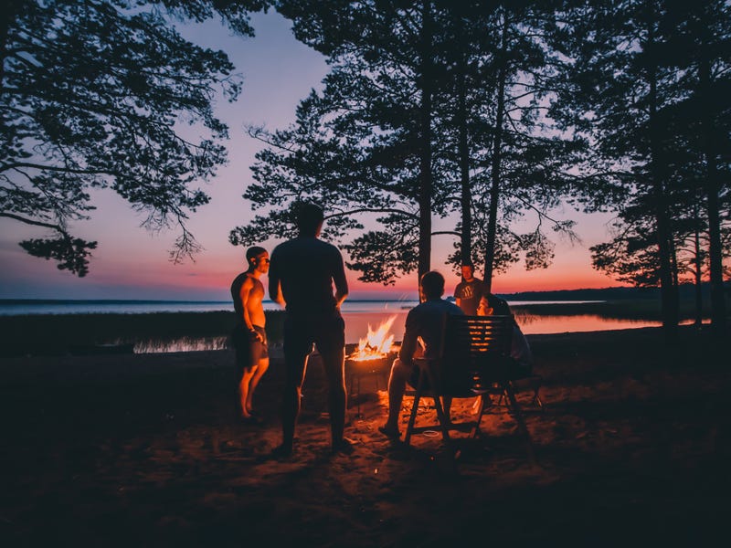People around a campfire near lake at sunset