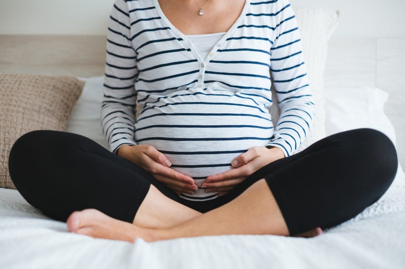 Pregnant woman in striped t-shirt sitting on the bed touching her belly