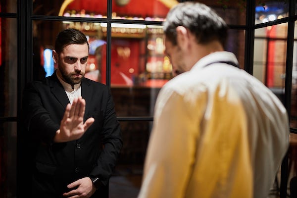 Portrait of restaurant security guard stopping drunk man from entering luxury establishment due to dress code