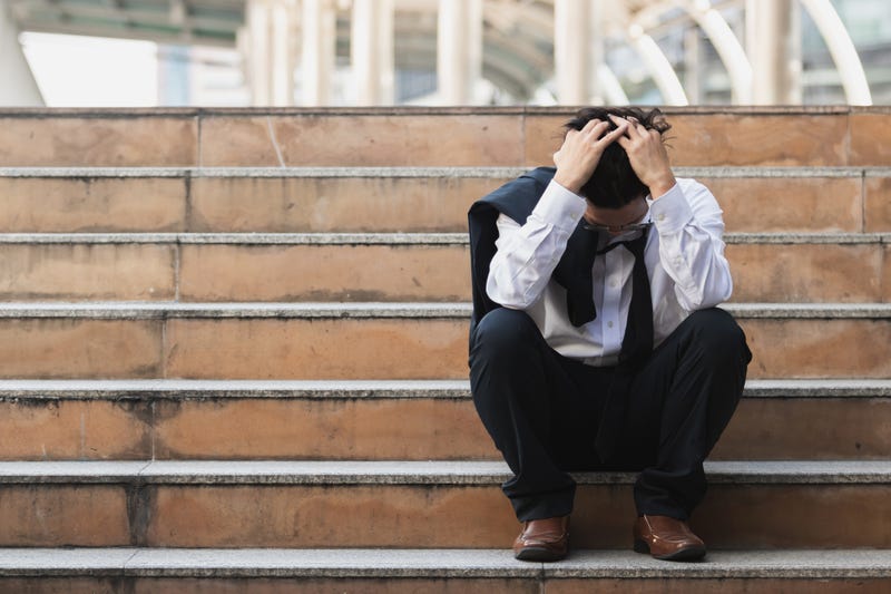 Frustrated man with his head in his hands, sitting on steps.