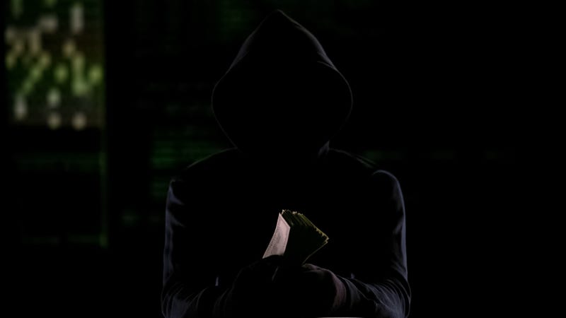 Hooded man in darkness holding cash, murder-for-hire reward or stolen money
