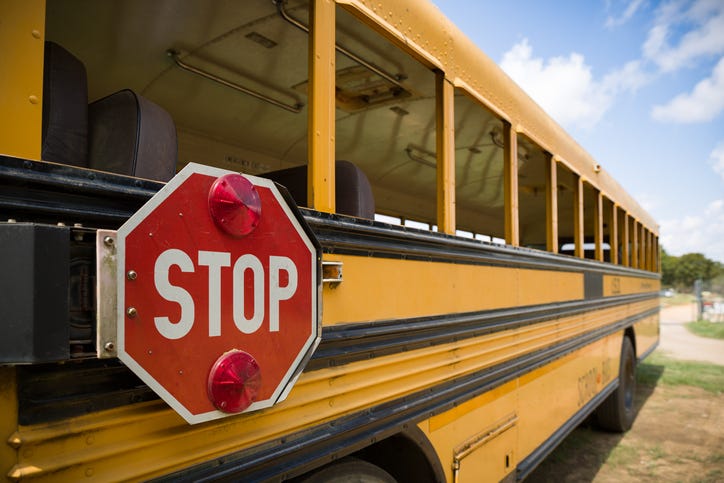 Exterior shot of the side of a school bus. The stop sign on the side of the bus is featured.